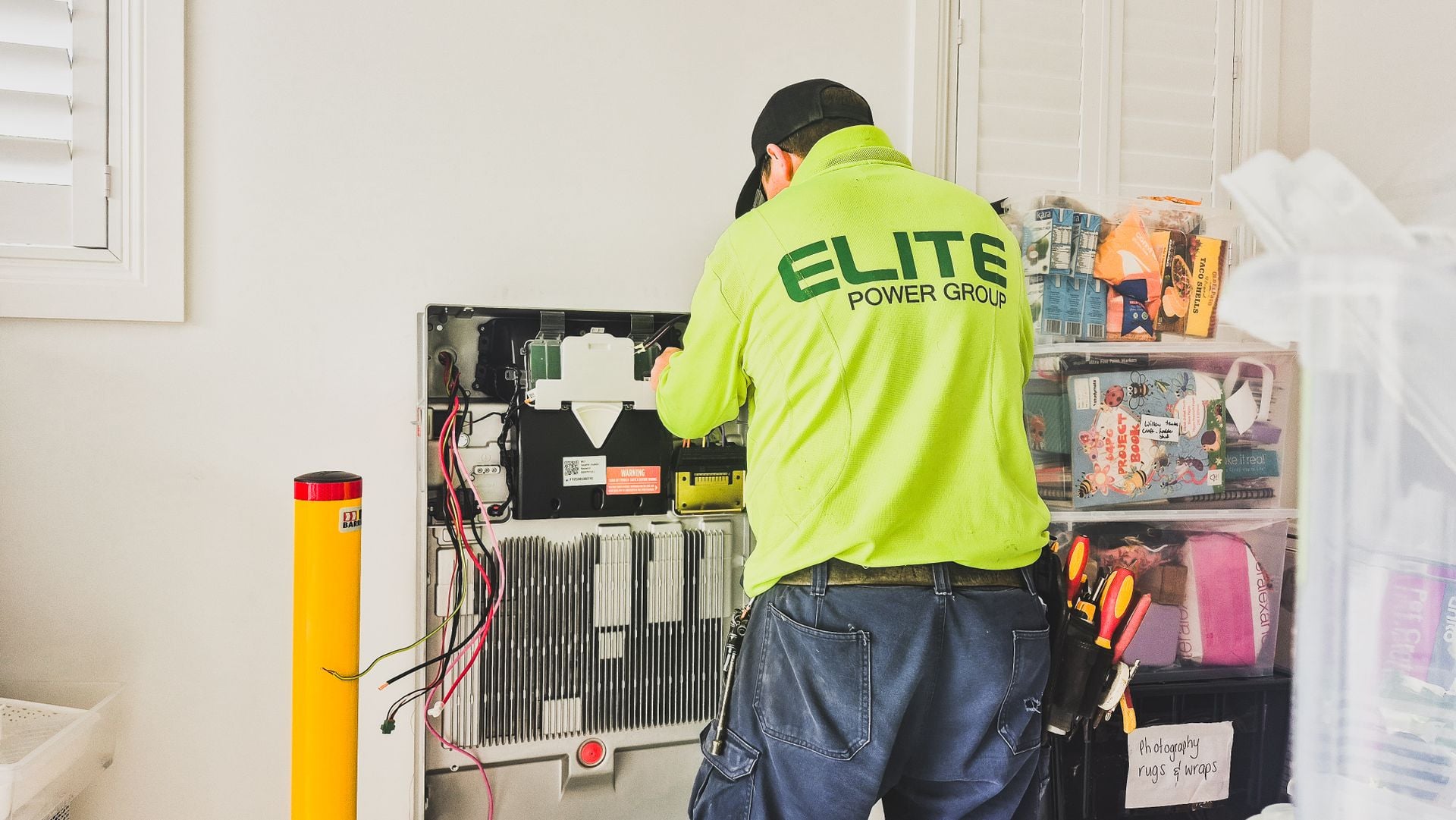An electrician working inside an open residential breaker panel in a garage