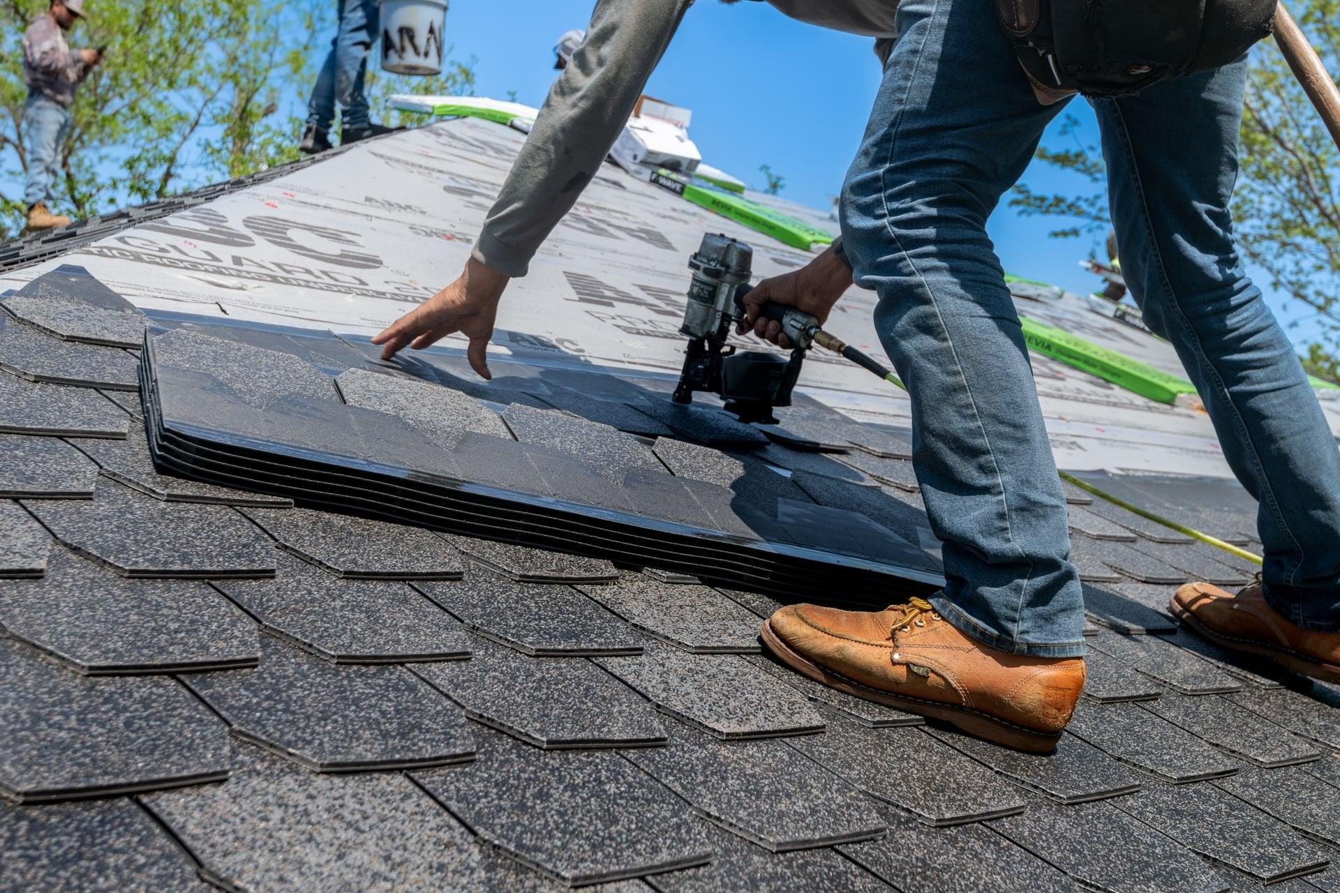 A roofer nailing down asphalt shingles with a coil nailer